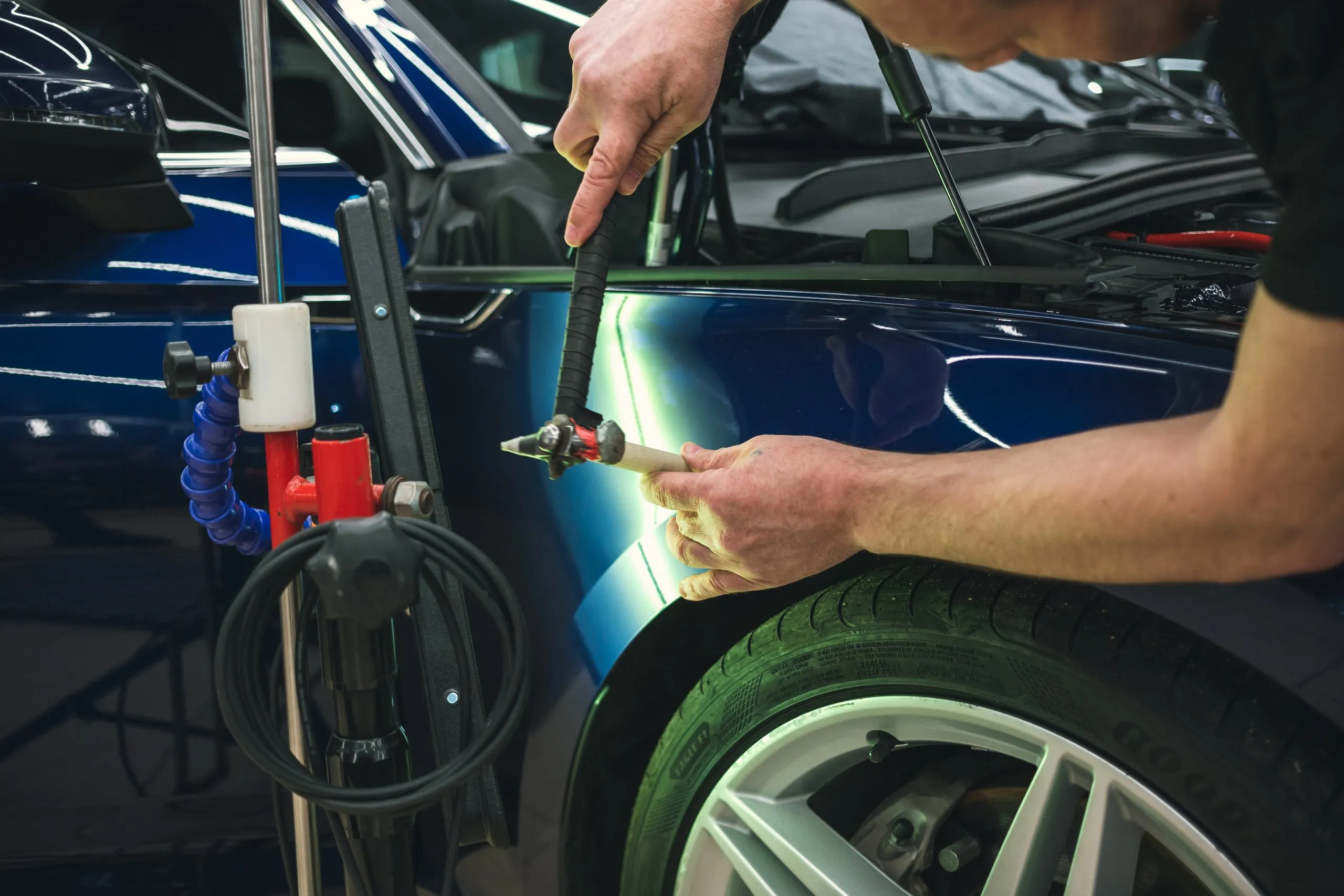 A technician performing paintless dent repair (PDR) on a car fender at Sandrof Auto Body.