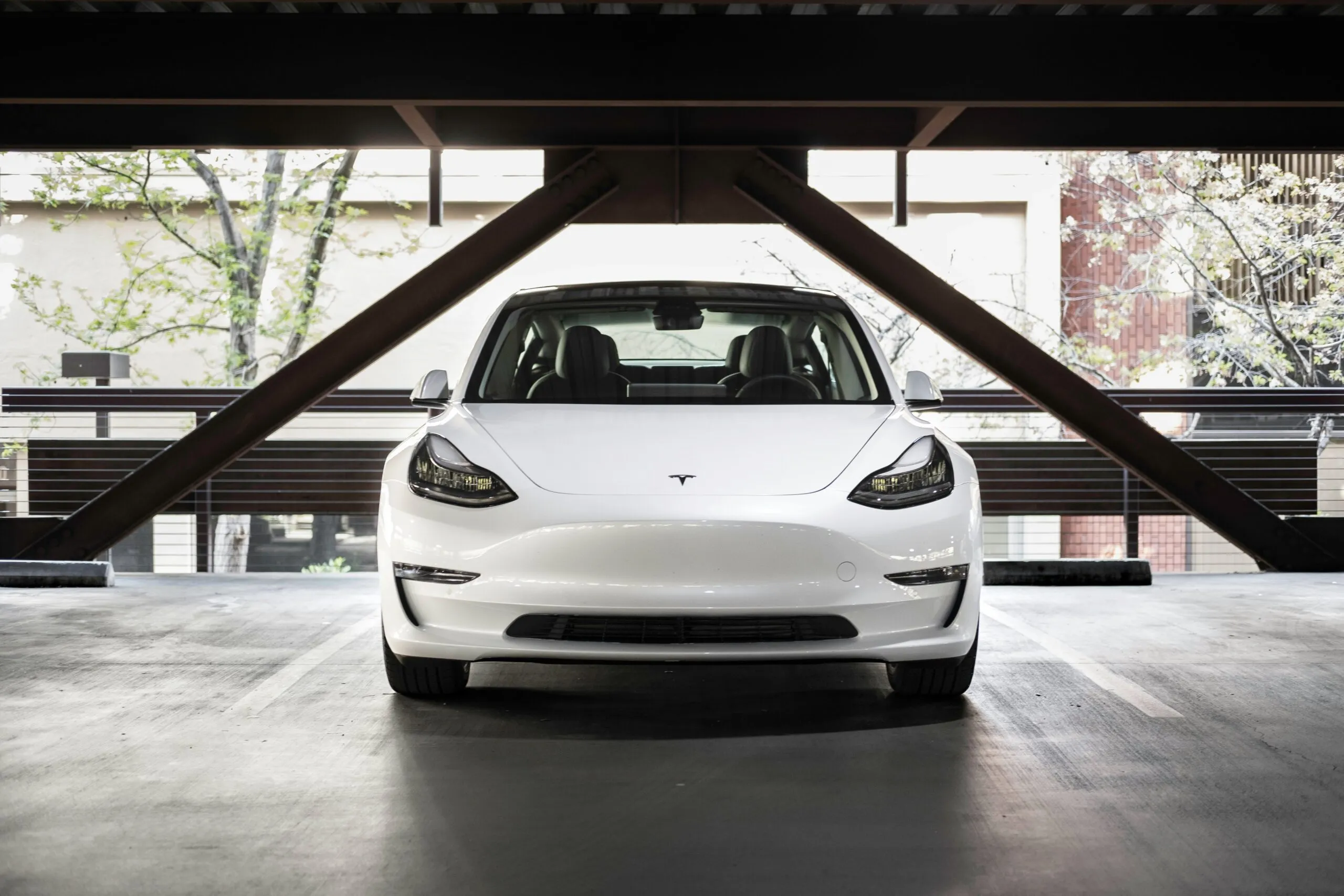 Front view of a white Tesla parked in the shade of a parking garage, showcasing its sleek and restored condition.