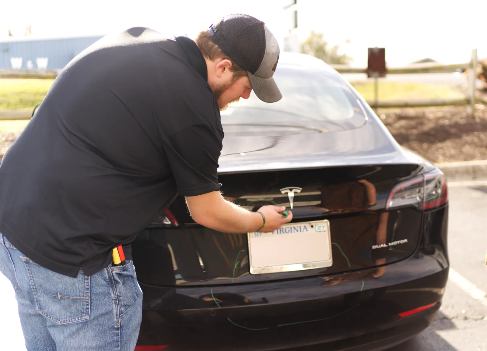 A technician inspecting the rear of a black Tesla Model 3 at Sandrof Auto Body, marking areas for repair.