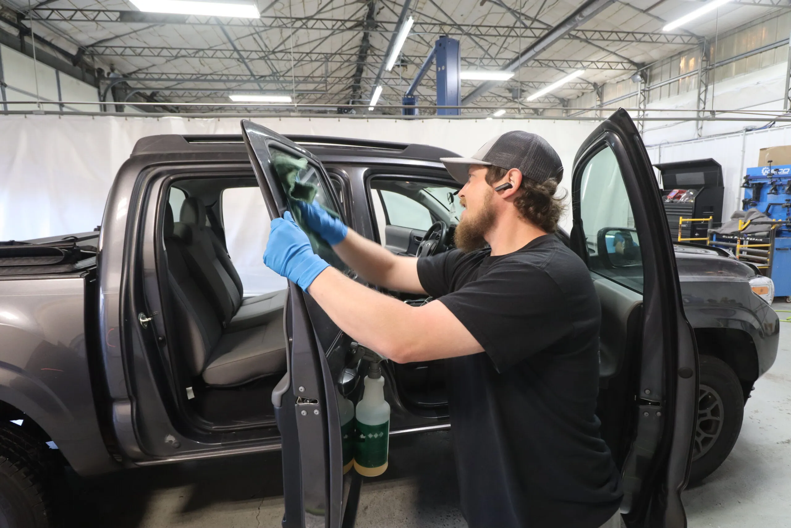 Technician carefully detailing the door panel of a gray pickup truck in a well-lit auto body shop.