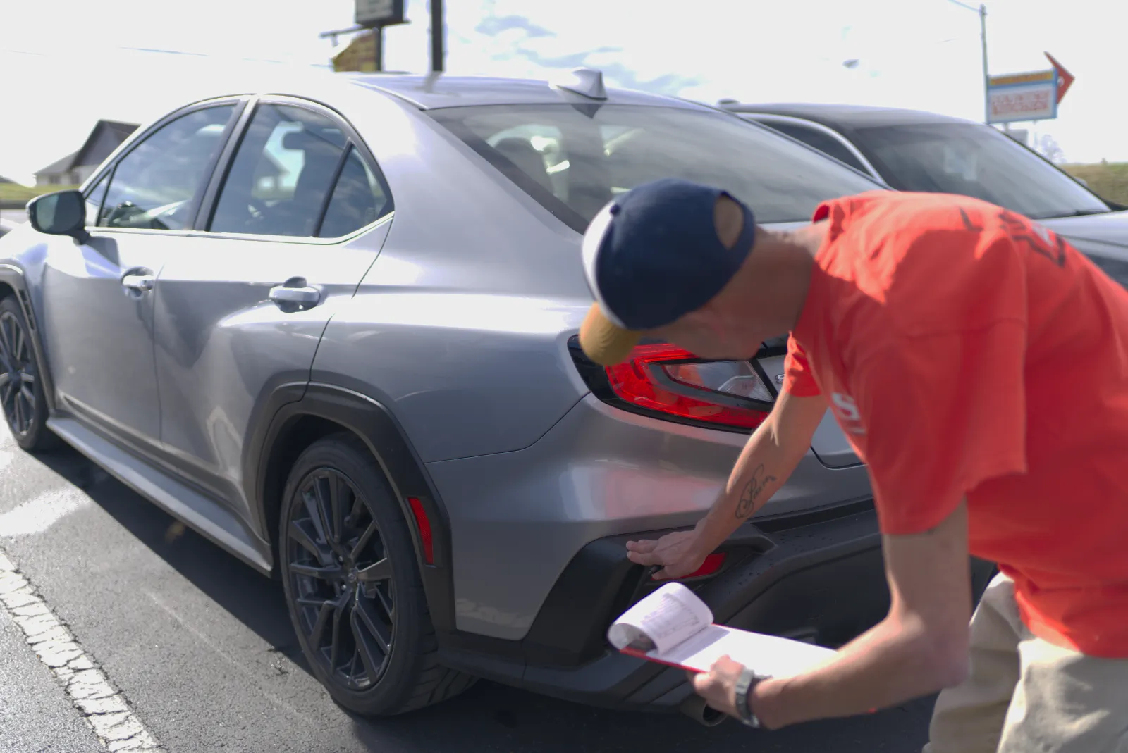 A technician inspecting a gray car’s rear bumper during a final quality check in bright daylight.