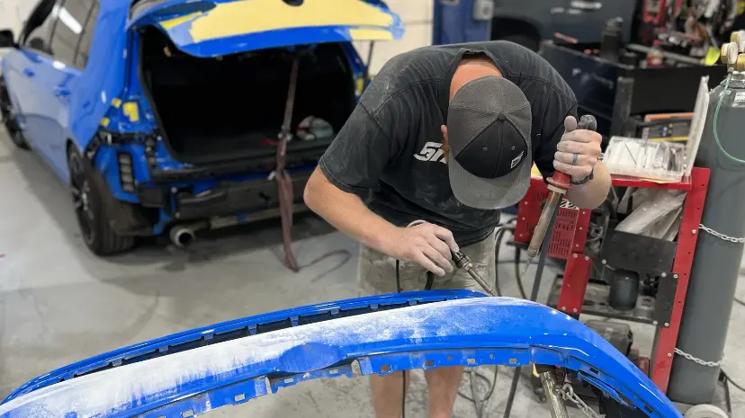 Technician repairing a vehicle bumper using plastic welding at Sandrof Auto Body.