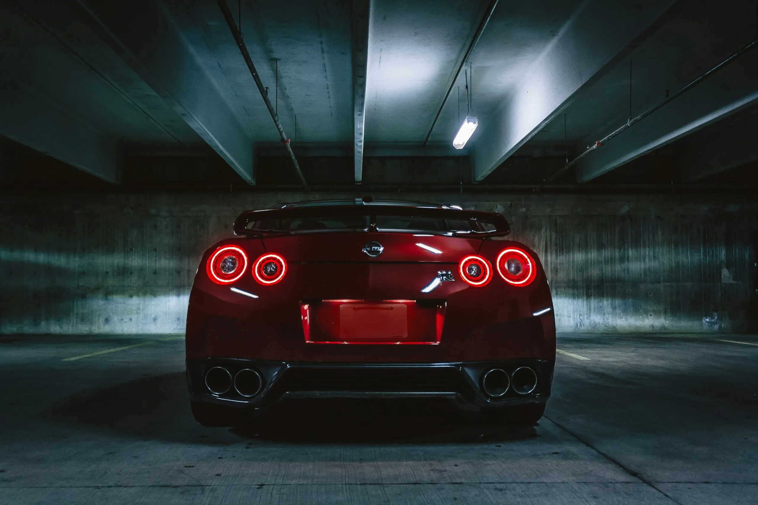 Rear view of a red sports car with illuminated circular tail lights in a dimly lit parking garage.