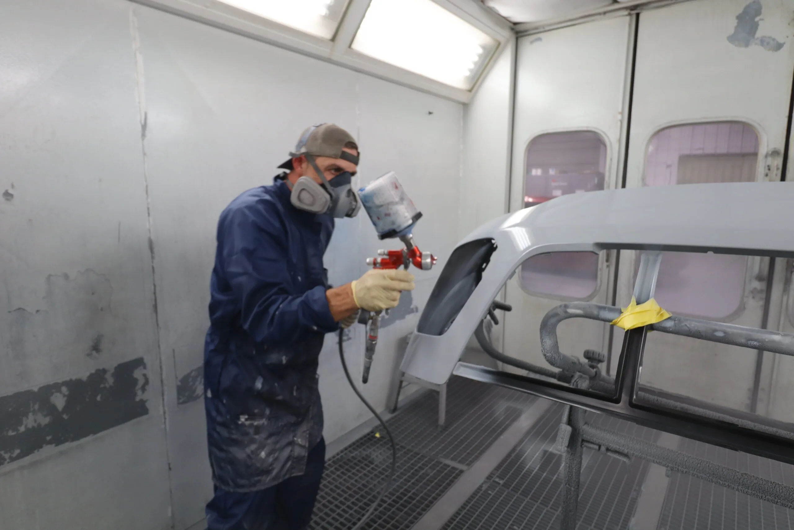 A professional automotive painter wearing safety gear spray painting a vehicle panel inside a paint booth at Sandrof Auto Body.