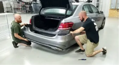 Two technicians installing a bumper on a vehicle at Sandrof Auto Body.