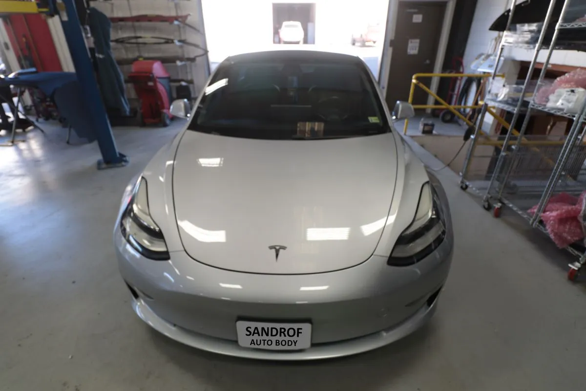 Silver Tesla completed after repairs, parked in the reassembly bay of an auto body shop.