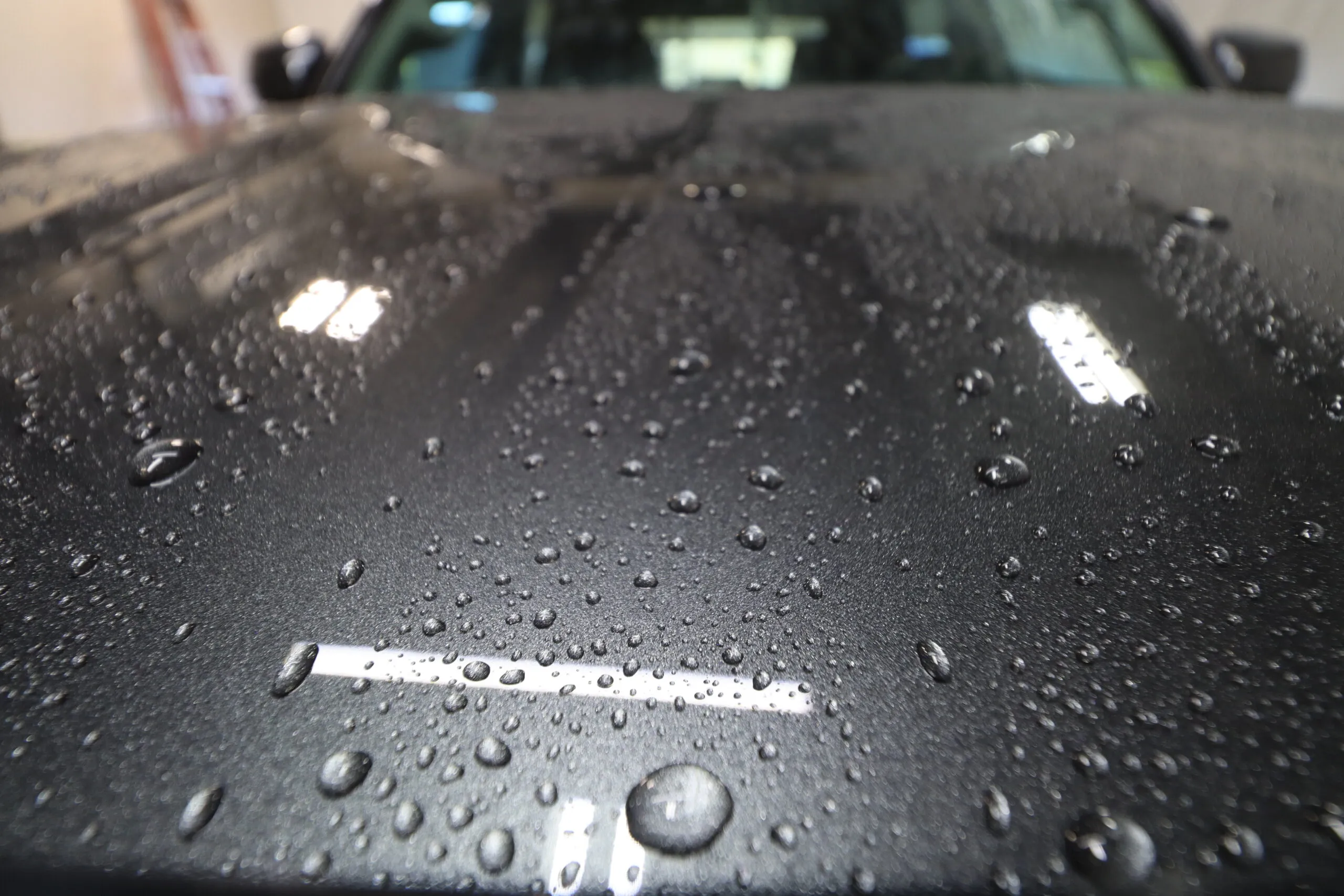 Close-up of a car hood with small water droplets, showcasing a sleek, glossy finish.